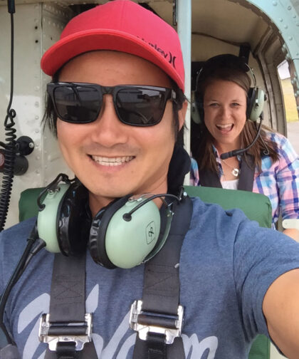 A man and woman sitting one in front of the other smile during a helicopter ride.