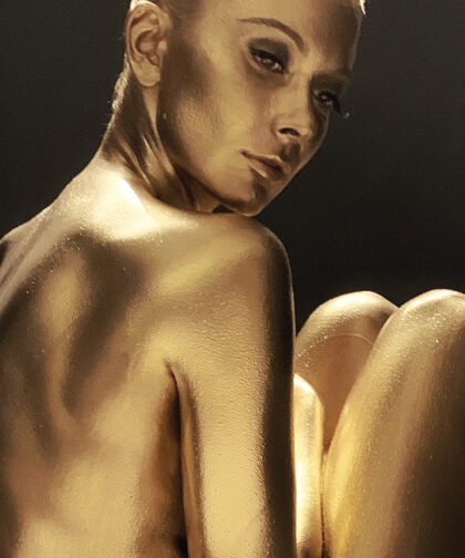 A woman painted gold looks over her shoulder.