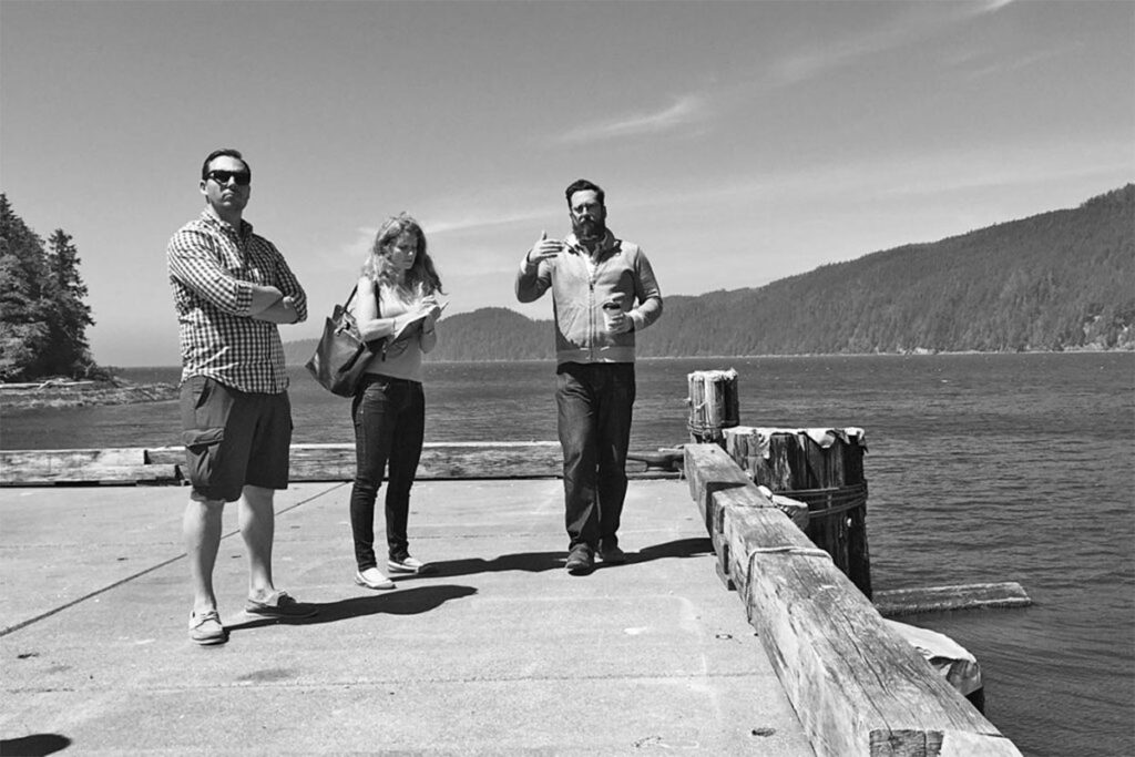 A black-and-white photo of three people conversing on a pier. 