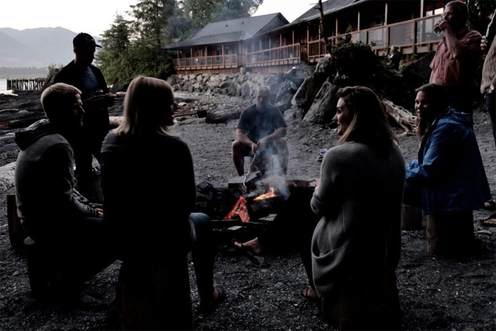 A group of people sit around an evening campfire. 