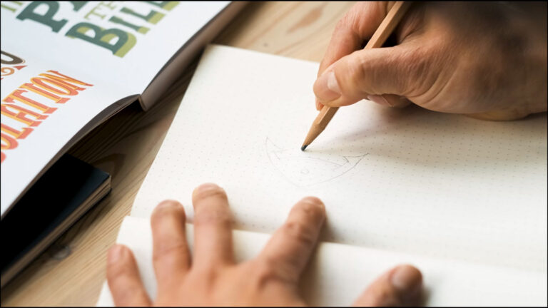 Someone sketches a logo in a notebook.