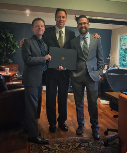 Three men in suits stand, holding a tabletop campaign book.