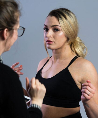 A model stands still as another woman stands in front of us, preparing her for the upcoming photoshoot.