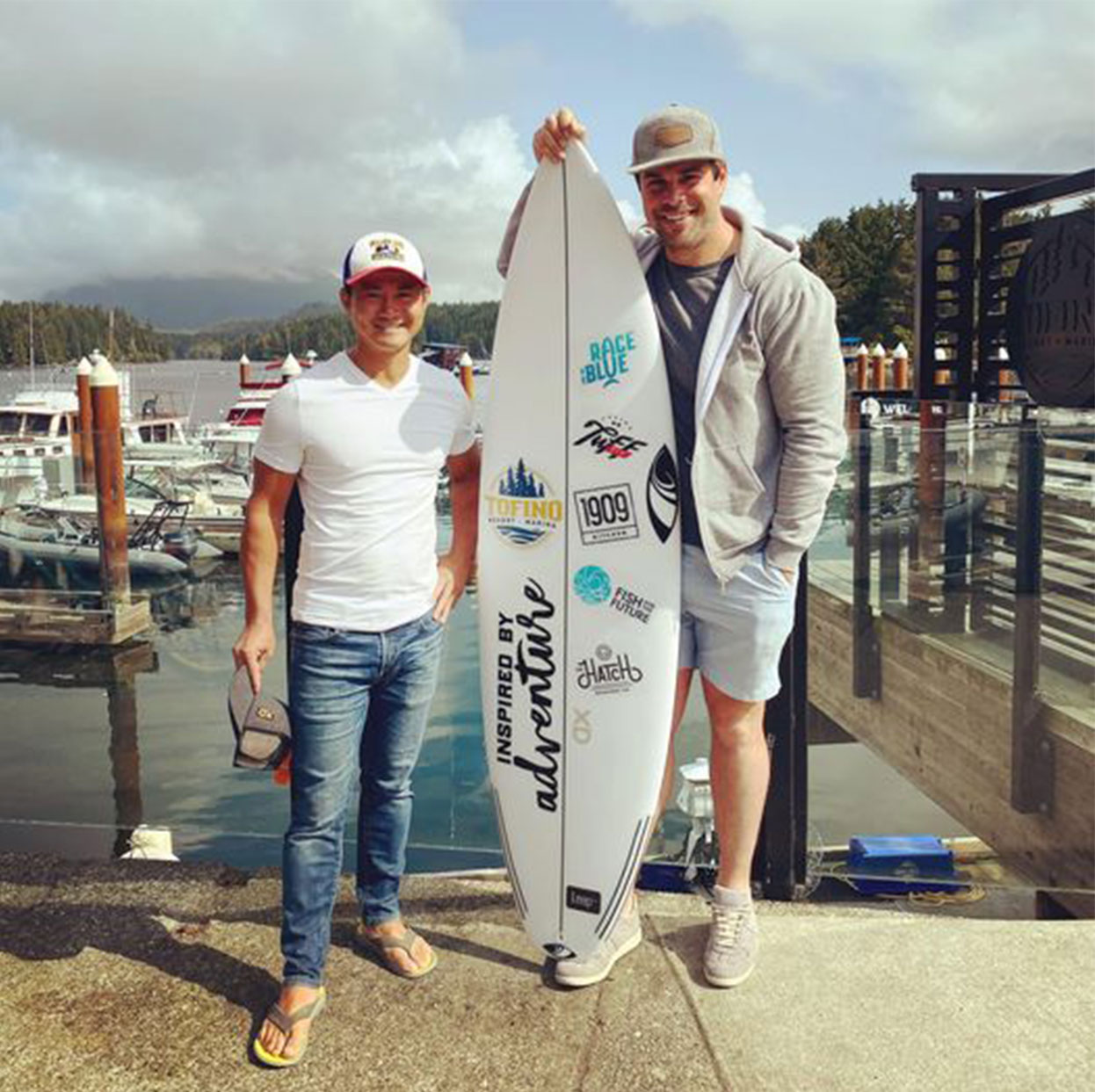 Neil Train and Willie Mitchell stand next to a surfboard bearing logos that Leap designed.