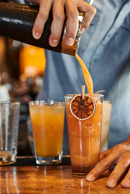 A close up of someone pouring an orange cocktail into a glass.