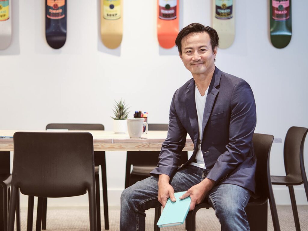 Leap XD owner Neil Tran sits in the studio board room, holding a notebook and gazing out at the viewer. 